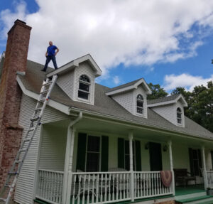 man stands on roof with ladder nearby Seamless Experts residential and commercial exterior remodeling Ozarks Missouri