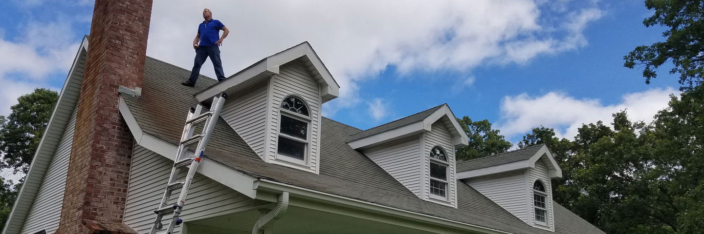 man stands on roof of home Seamless Experts residential and commercial exterior remodeling Ozarks Missouri